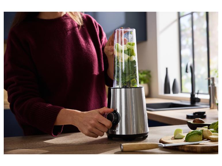 Vrouw gebruikt een blender met fruit en groenten voor een smoothie in de keuken.