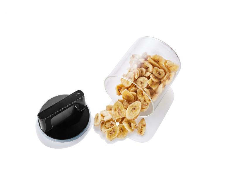 Gedroogde bananenplakjes in een glazen pot met een plastic deksel.