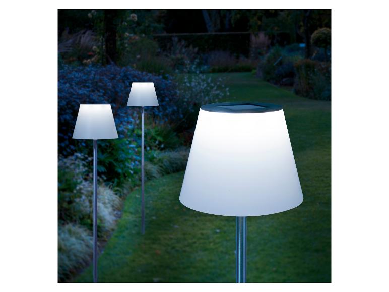 Drie verlichte solar tuinlampen in een tuin bij schemering.