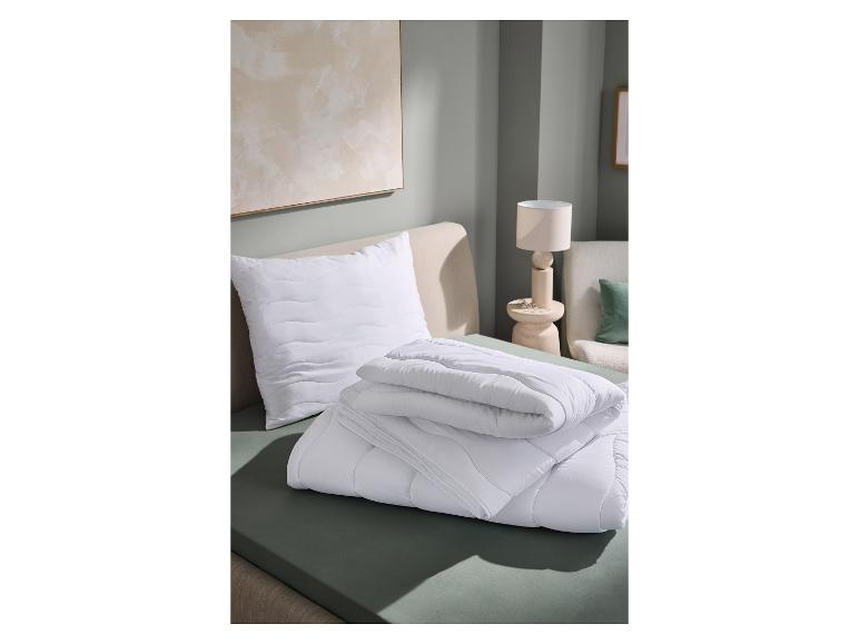 Wit gewatteerd kussen en opgevouwen dekbed op een bed met groene lakens.