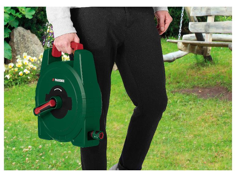 Persoon die een groene slanghaspel met rood handvat vasthoudt in een tuinomgeving.