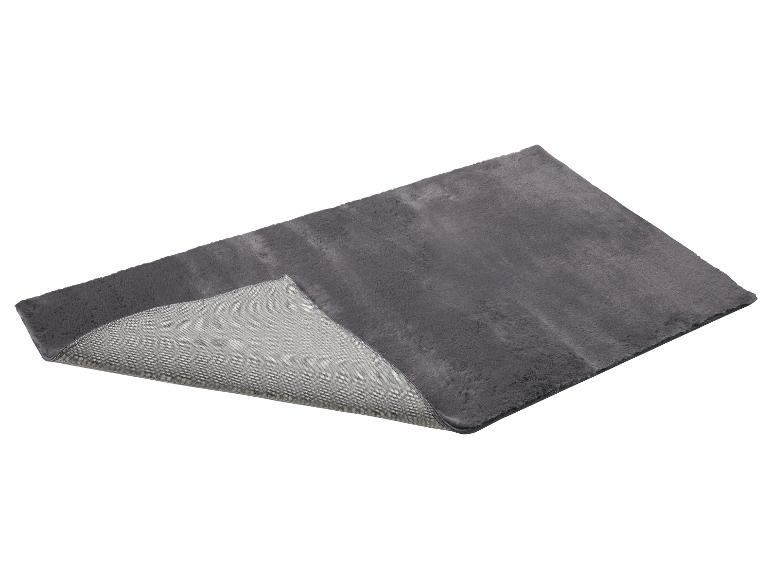 Grijs pluizig vloerkleed met antislip onderkant, deels opgevouwen.