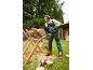 Vrouw in beschermende kleding zaagt boomstammen met een kettingzaag op een zaagbok in een tuin.