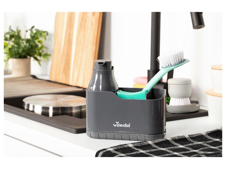Grijze gootsteenorganizer met zeepdispenser, borstel en spons in een moderne keuken.