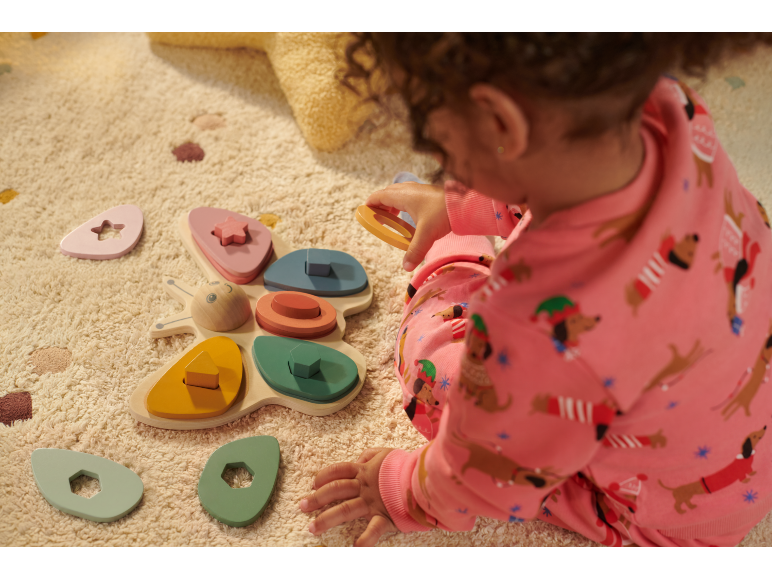 Baby speelt met houten vlindervormige sorteerspeelgoed op een licht tapijt.