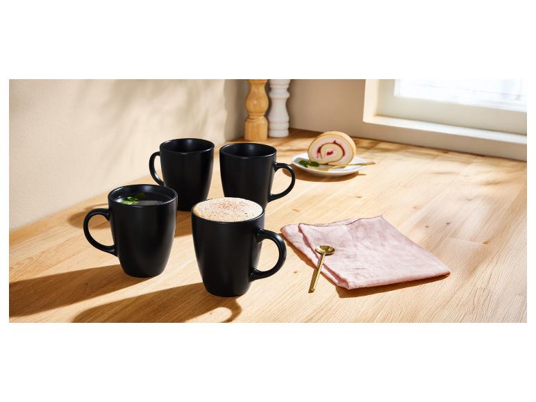 Drie zwarte mokken en een cake roll op een houten tafel.