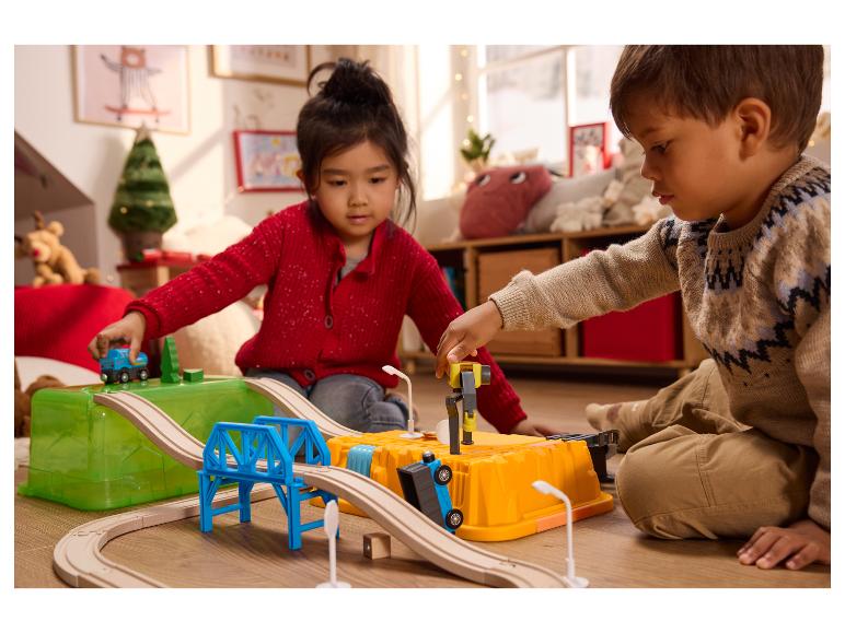 Twee kinderen spelen met een houten treinset en speelgoedauto's op de vloer.
