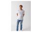 Man in wit T-shirt met tekst en blauwe jeans, handen in zakken.