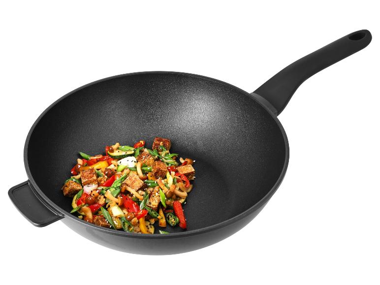 Zwarte metalen wok met handvat, gevuld met roergebakken groenten en tofu.