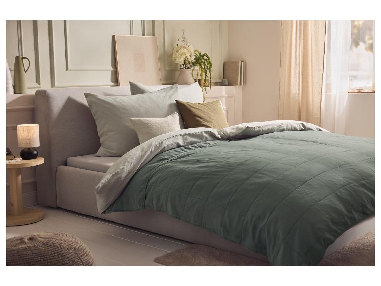 Slaapkamer met een bed met een groene gewatteerde sprei en lichte kussens.