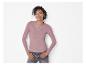 Lachende vrouw in roze shirt met lange mouwen en jeans, draagt zilveren sieraden.