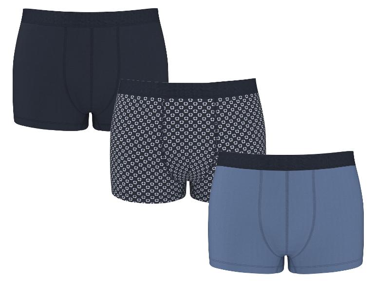 Verpakking van drie heren katoenen boxershorts: één marineblauw, één met geometrisch patroon en één lichtblauw.