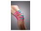Een knie met roze en blauwe kinesiotape op een grijze achtergrond.