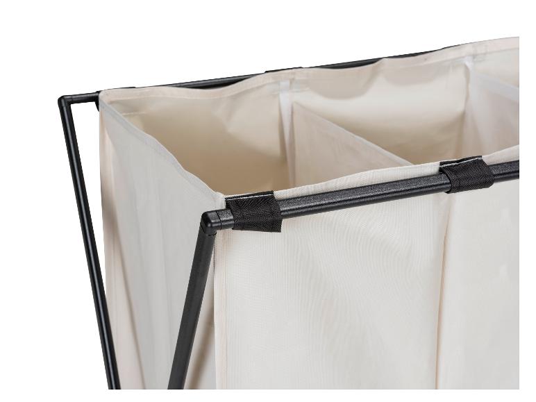 Close-up van een beige wasmand met drie compartimenten en een zwart metalen frame.
