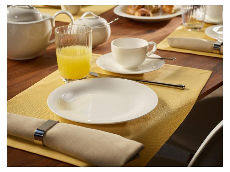 Ontbijttafel met witte borden, kopjes, kan, glas sap en servetten.