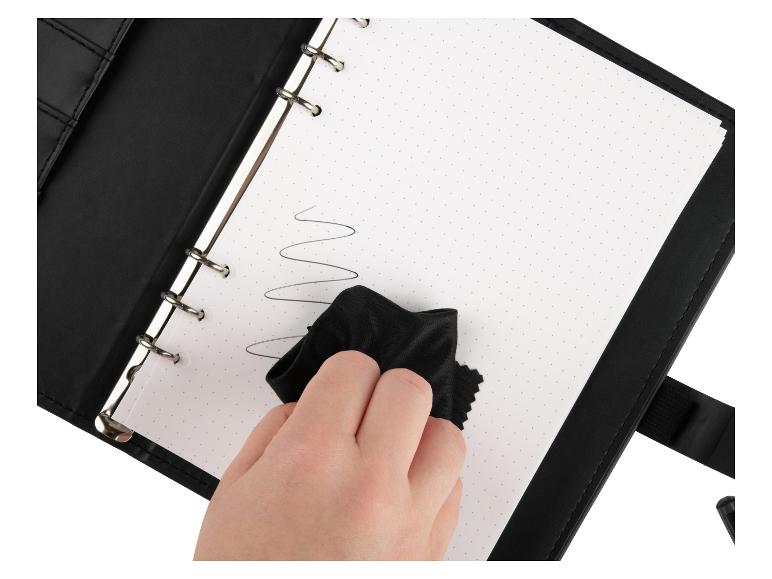 Een zwart ringband schrift wordt met een doekje schoongemaakt.