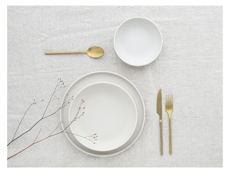 Wit serviesgoed, gouden bestek en minimalistische decoratie.