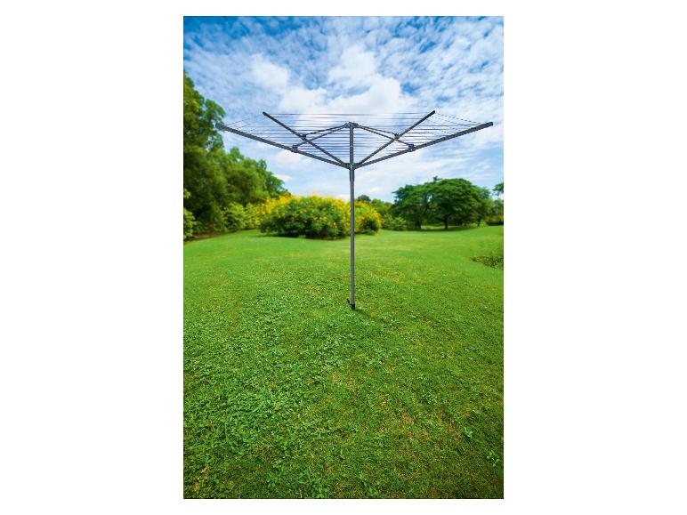 Vierarmige droogmolen op een groen gazon met bomen en bloemen op de achtergrond