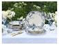 Elegante buitentafelsetting met blauw-wit bloemig servies, gouden bestek en witte bloemen.
