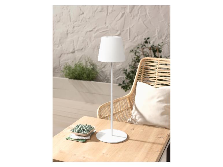 Moderne witte tafellamp op een houten tafel, naast een rotan stoel.