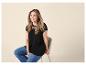 Lachende vrouw in zwart kanten T-shirt en jeans, zittend op een kruk.