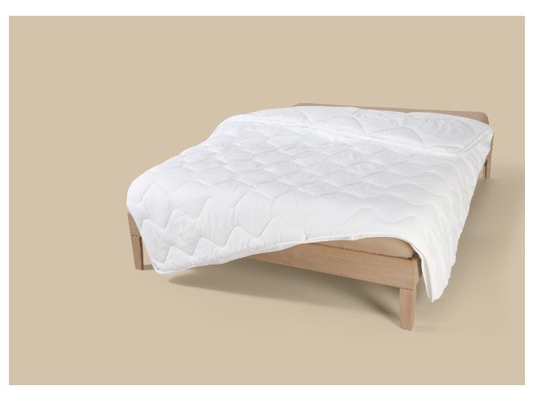 Wit gewatteerd dekbed op een licht houten bedframe.