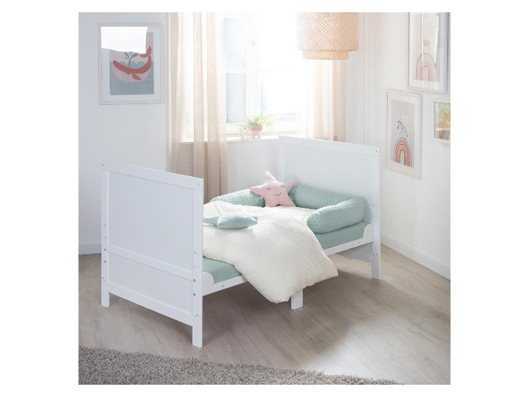 Wit kinderbedje met mintgroen beddengoed en sterrenkussens in een lichte kinderkamer.