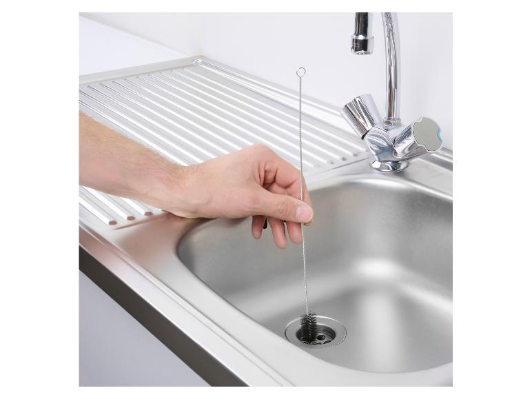 Hand reinigt gootsteen met een flessenborstel.