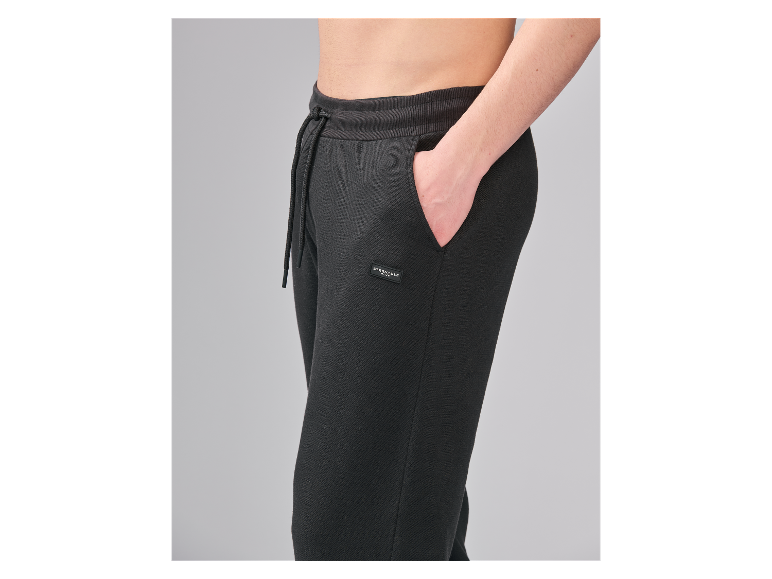Close-up van een persoon die een zwarte joggingbroek draagt met een trekkoord en een klein label.