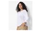 Vrouw in witte geborduurde blouse en beige broek.