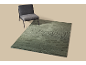 Een grijze stoel naast een groen vloerkleed met een wervelend patroon op een beige achtergrond.