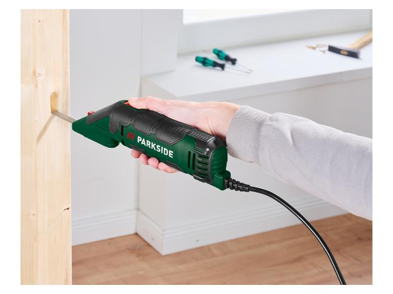 Een hand houdt een elektrische beitel vast die een gat in een houten balk snijdt.