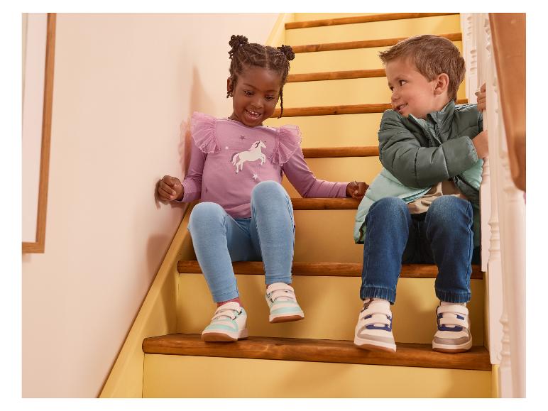 Twee kinderen zitten op de trap, gekleed in een paarse longsleeve en een groene jas.