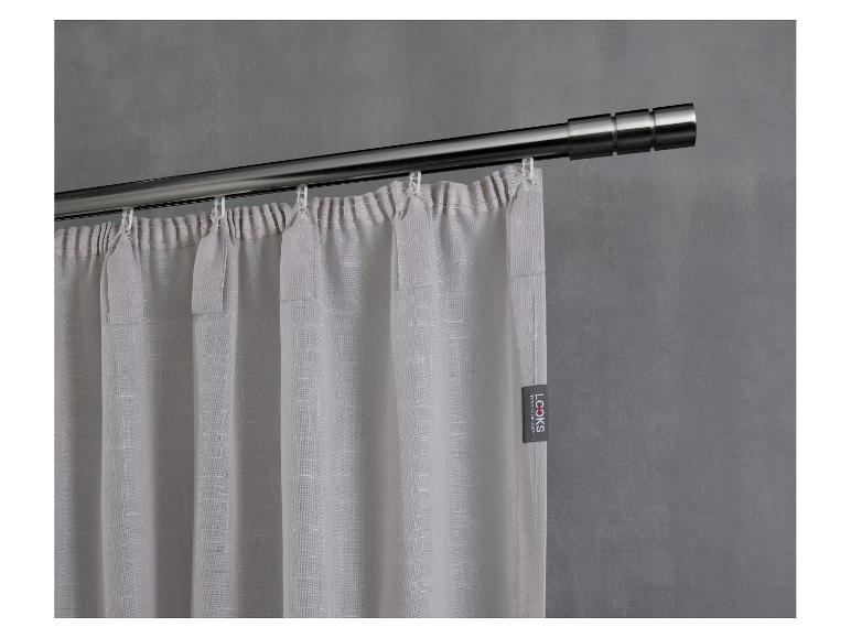 Lichtgrijs gordijn van getextureerde stof, hangend aan een zilveren roede tegen een donkere muur.