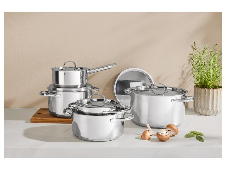 Set glanzende roestvrijstalen potten en pannen op een aanrecht met champignons en kruiden.