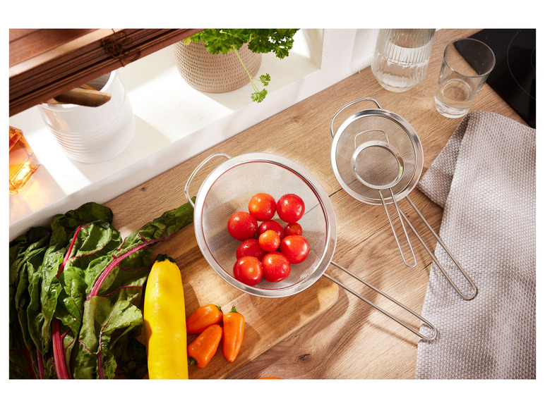 Drie metalen zeefjes met een kom vol cherrytomaatjes