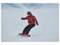 Snowboarder in rood patroonjack en zwarte broek, op een rood snowboard.