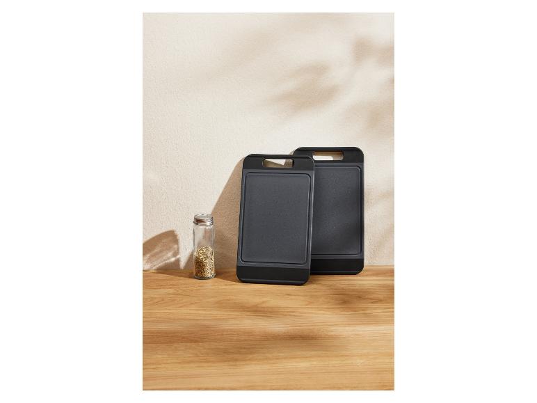 Twee zwarte snijplanken en een kruidenpotje op een houten tafel.