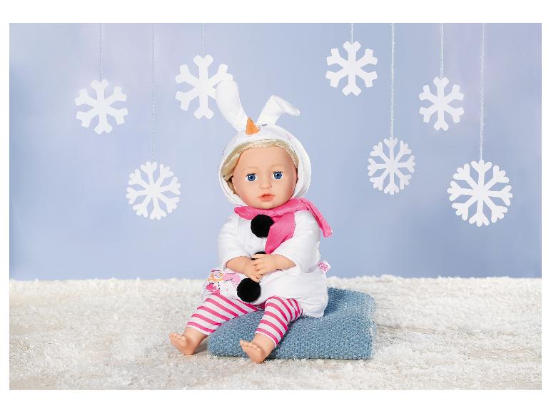 Pop in sneeuwmanoutfit met roze sjaal, zittend op een blauwe deken tussen sneeuwvlokken.