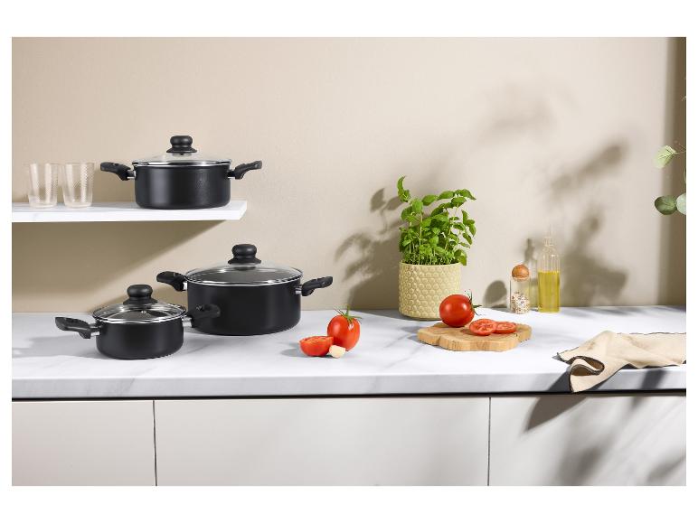 Zwarte kookpotten met glazen deksels, verse tomaten, basilicum en keukenaccessoires.