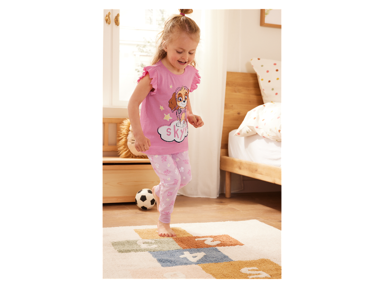 Een meisje in Paw Patrol pyjama speelt op een kleed.