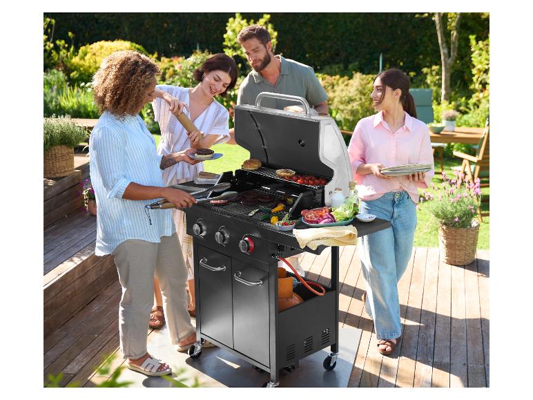Vier vrienden grillen hamburgers en groenten op een Grillmeister gasbarbecue in een tuin.