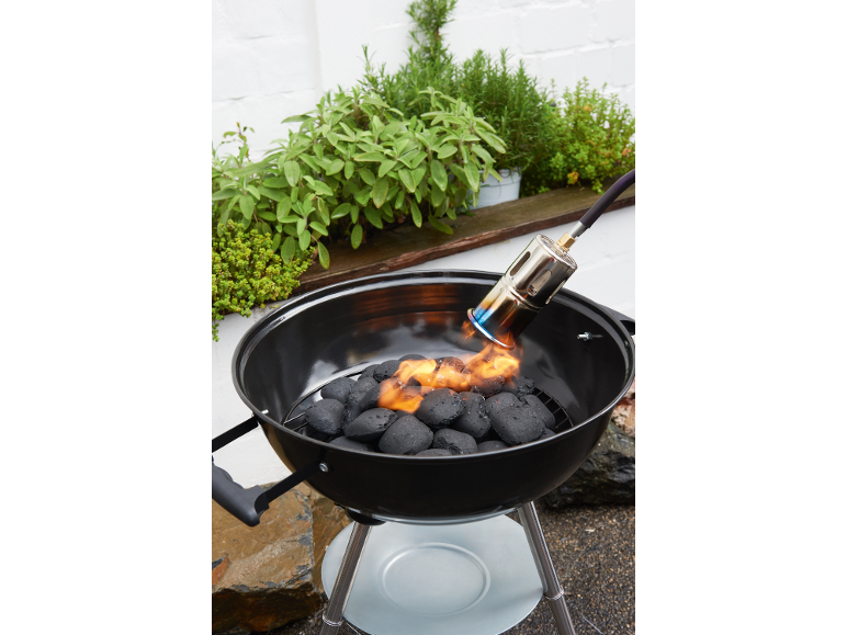 Houtskoolbarbecue met aansteker, omringd door kruidenplanten.