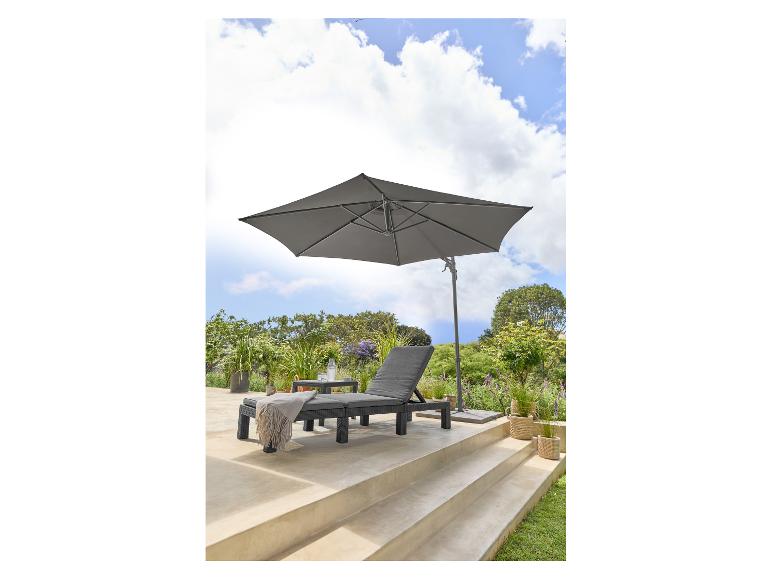 Grijze tuinparasol en ligstoel op een terras met weelderig groen.
