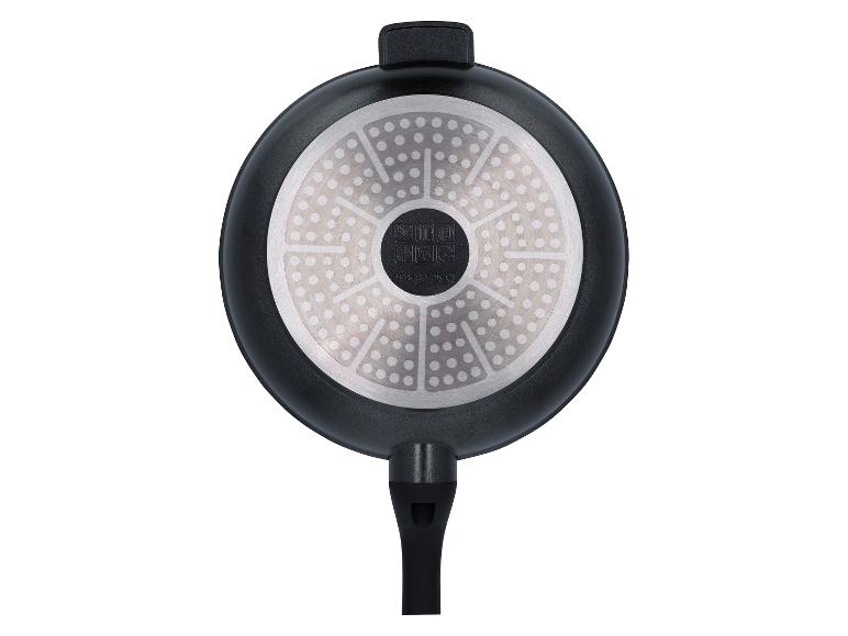 Onderkant van een zwarte koekenpan met een zilveren, gestippelde inductiebodem en een zwart handvat.