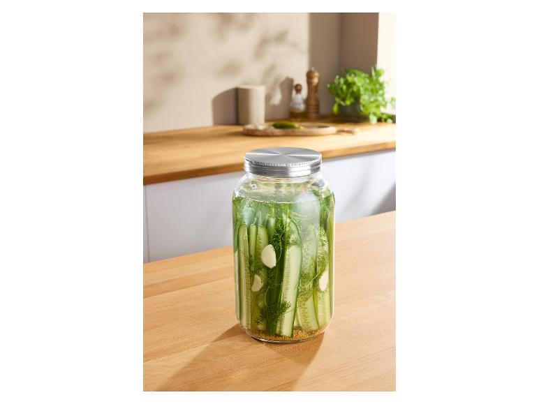 Augurken in een glazen pot met metalen deksel op een houten aanrecht.