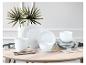 Witte serviessets op een lichte houten tafel met decoratieve palmbladeren.