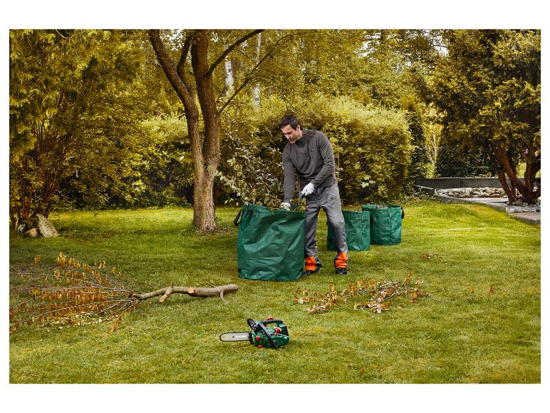 Man ruimt takken op in groene tuinzakken, met een kettingzaag ernaast.