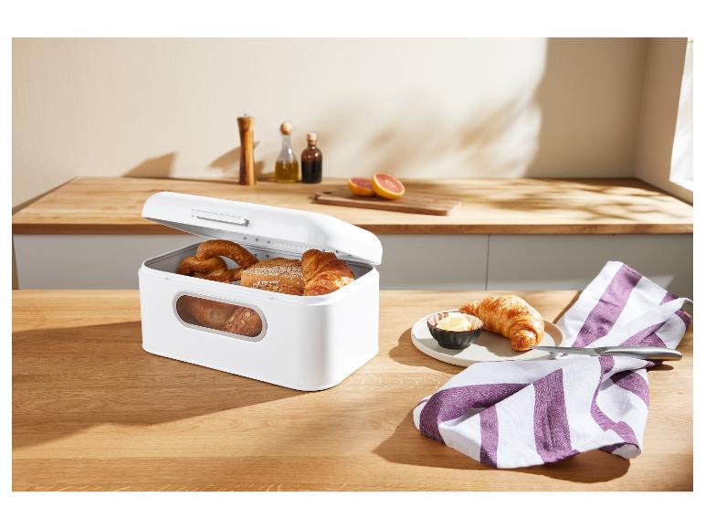 Witte broodtrommel gevuld met gebak op een houten tafel, met een croissant en boter.