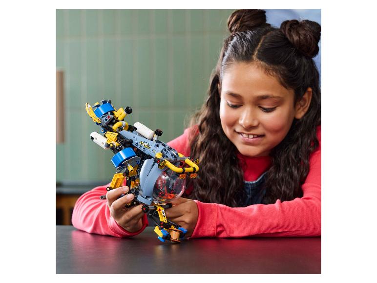 Een lachend meisje houdt een gele en blauwe LEGO Technic onderzeeër vast.